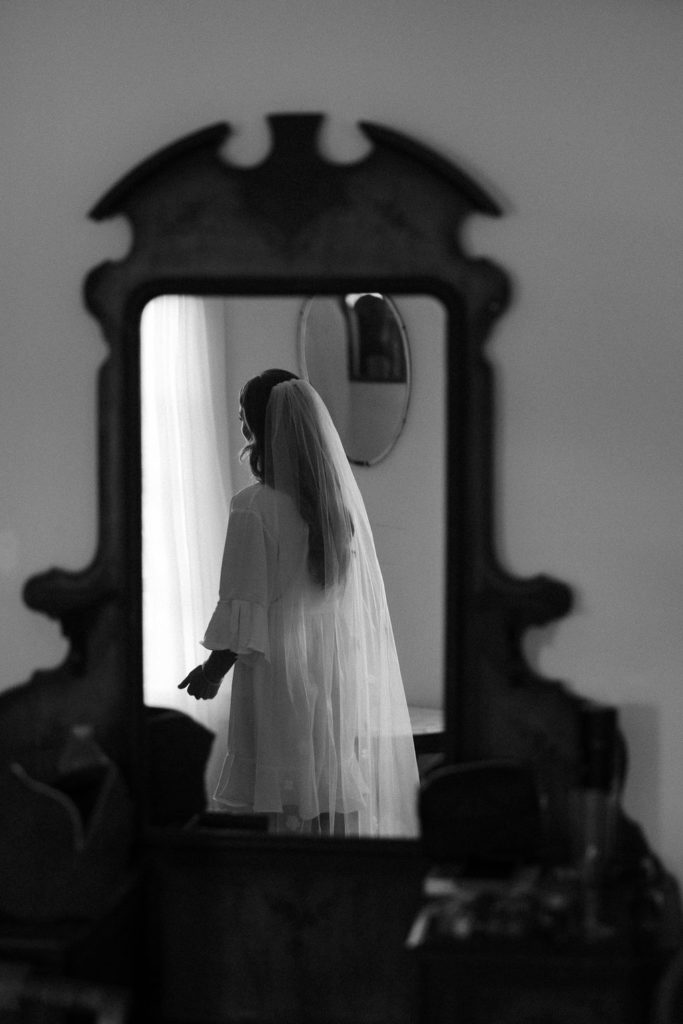 bride in dressing gown wearing a veil in a blurry reflection of a mirror