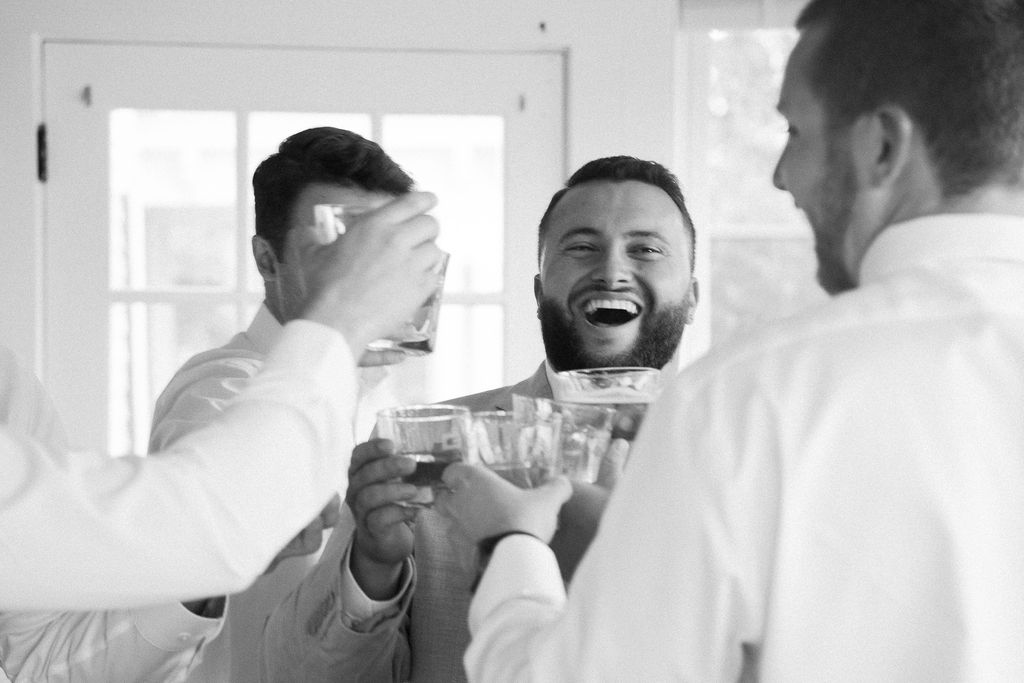 groom laughing as he toasts with his groomsmen before the wedding