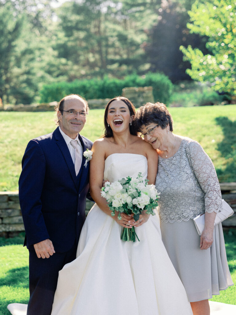 Fun family portrait of bride, her father, and her grandmother laughing before her wedding ceremony on a sunny day in Maine.