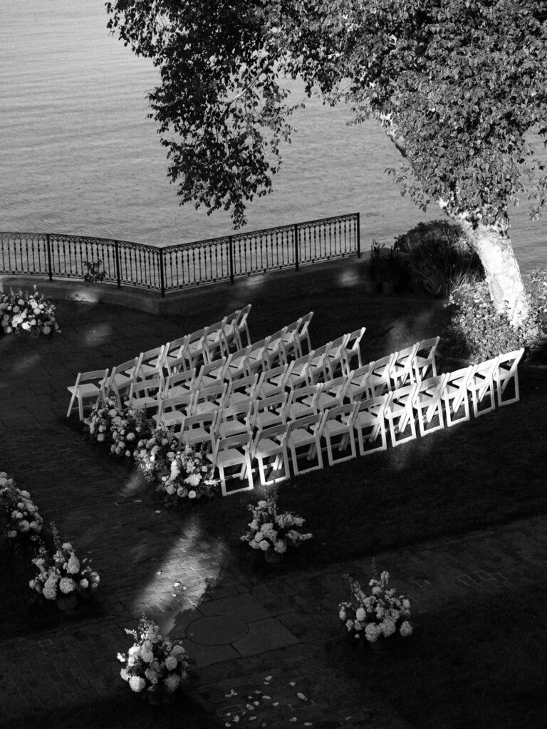 Elevated view of a ceremony location, flowers, and chairs while being lit with dappled light. on a wedding day overlooking the ocean.