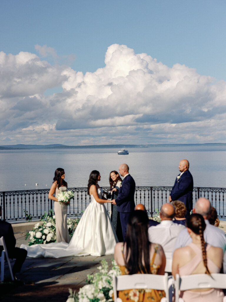 Bride and groom hold hands during a wedding ceremony overlooking the ocean at the Bar Harbor Regency in Maine.