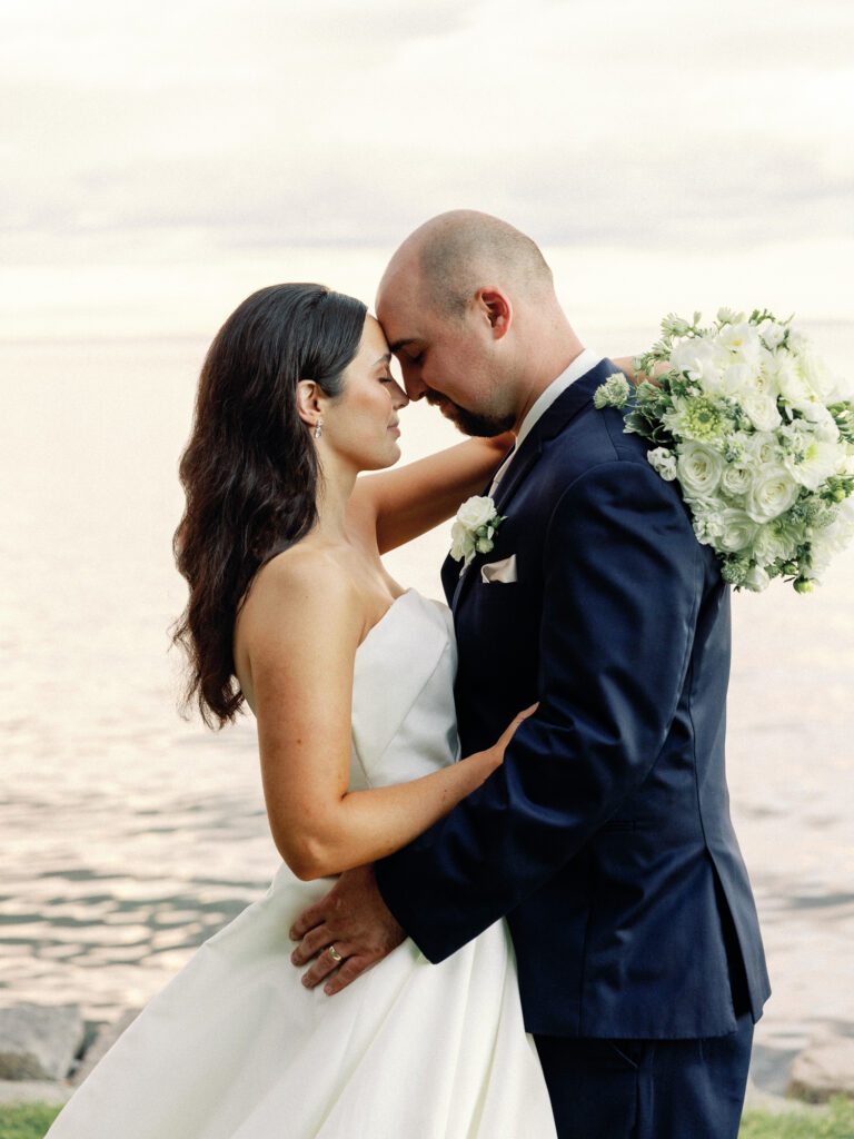 Bride and groom nestle into each other, touching foreheads in a sweet wedding pose after their ceremony on the ocean.