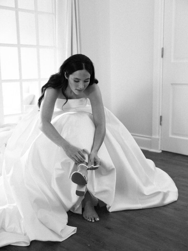 Bride wearing ballgown puts on her shoes before her wedding ceremony.