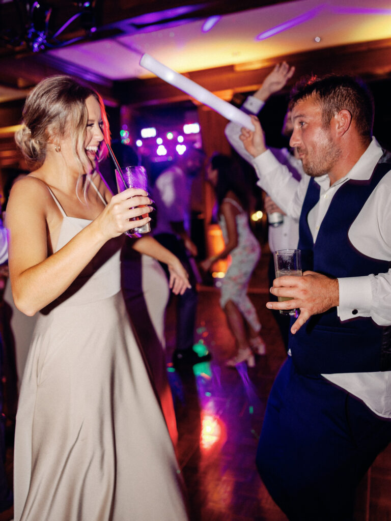 Fun flash photography during wedding reception of couple dancing while multi-colored DJ lights strobe in the background.