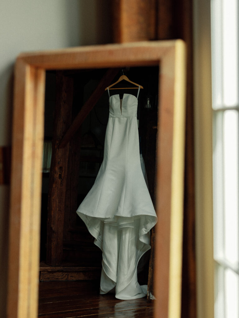 Strapless wedding dress is reflected in a mirror while the bride waits to get dressed.
