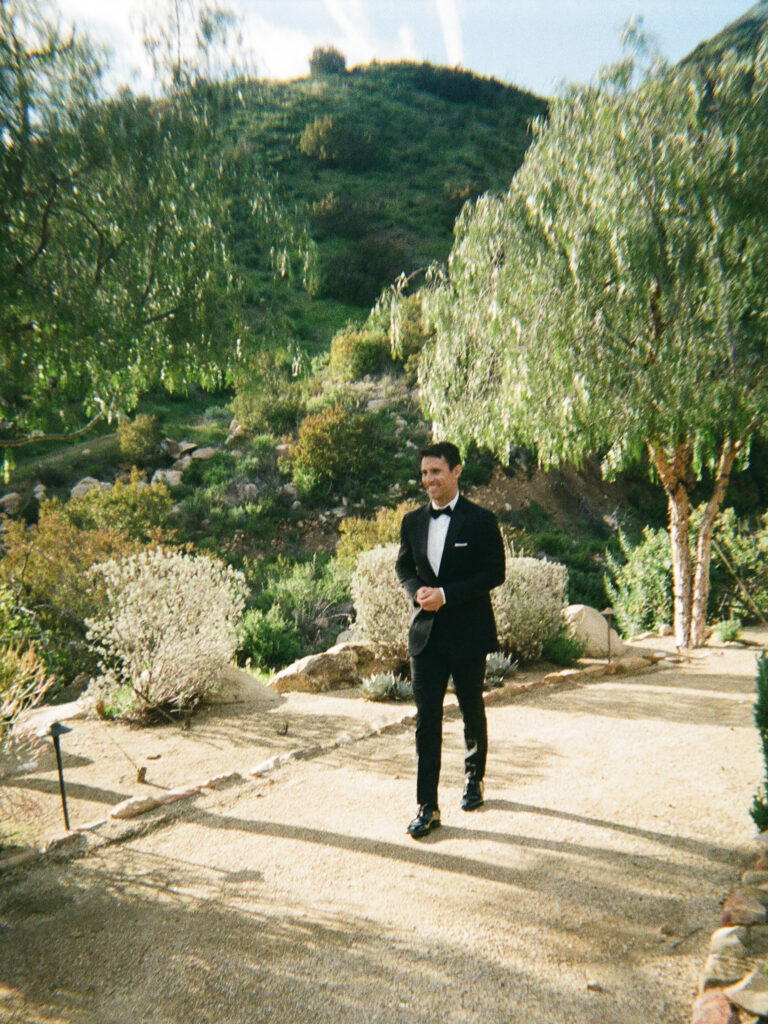 Groom in a black tux and bowtie walks toward the wedding ceremony.