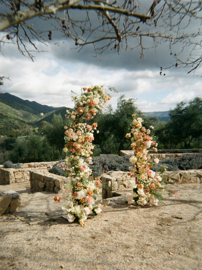 Asymmetrical flower arch made with peach, terracotta, and white flowers as crafted by Creative Light Design.