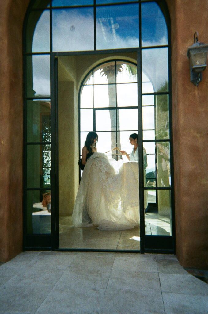 Bride and maid of honor move a large wedding gown through the house.