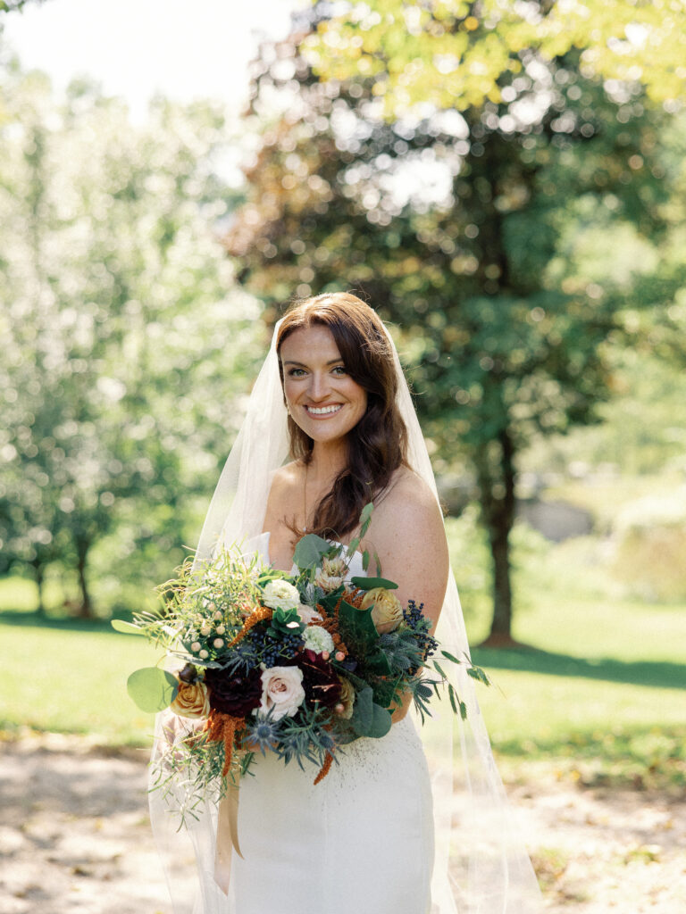 Sunny bridal portrait at a fall wedding with a bride wearing a long veil and holding an autumn bouquet. 