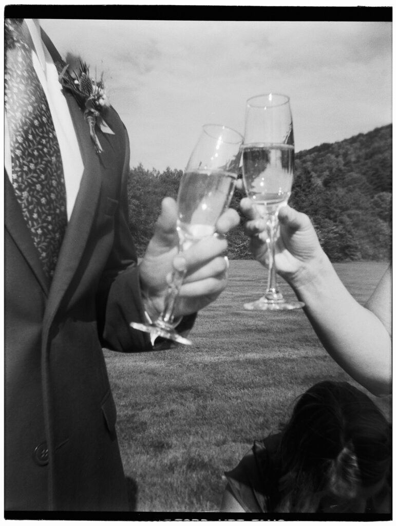 Fun wedding photos from disposable cameras are a new trend (from an old era). This film image, by Burlington wedding photographer Kay Cushman, shows a bride and groom holding champagne.