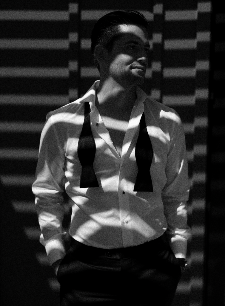 Moody photo of groom during wedding while getting dressed. Streaks of light cut across him in black and white.