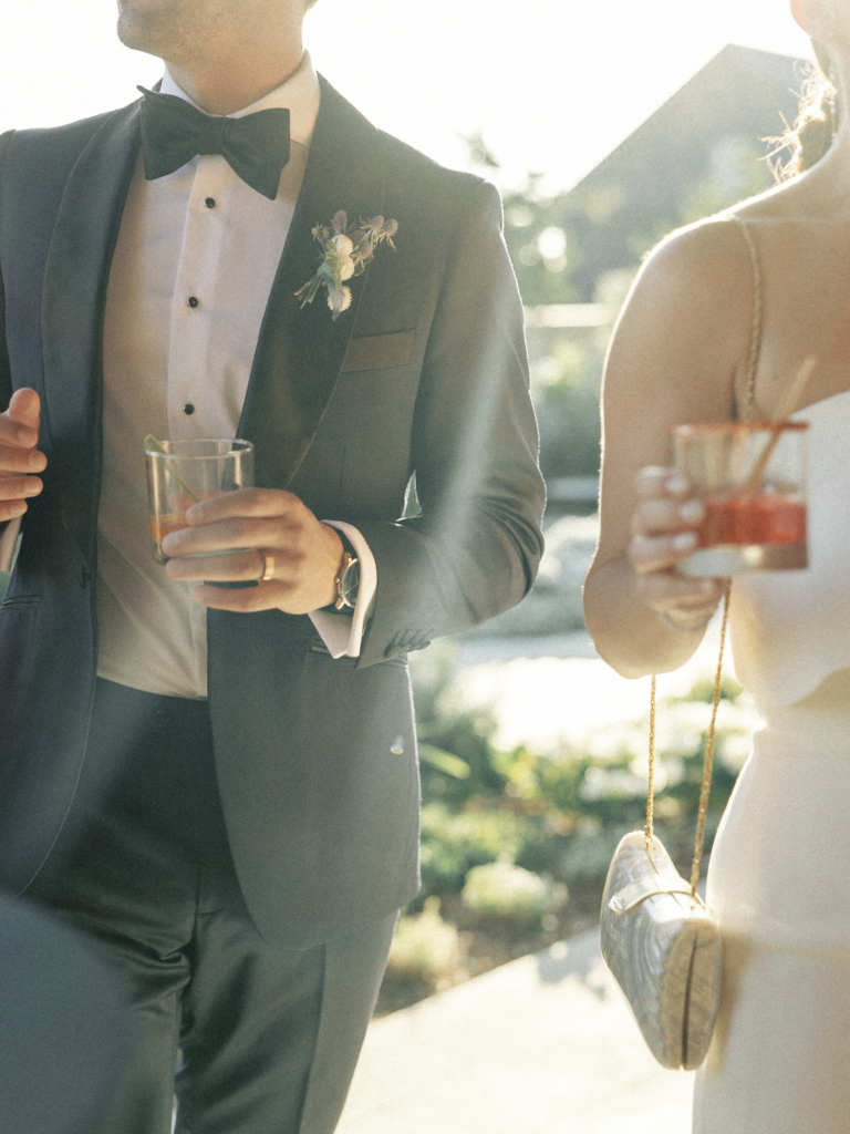 Candid photo of bride and groom holding cocktails while backlit by the sun during their black tie wedding in Napa Valley.