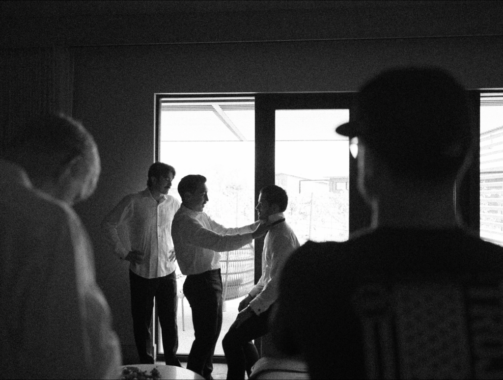 Black and white groom getting dressed surrounded by his groomsmen. Black and white film photography.