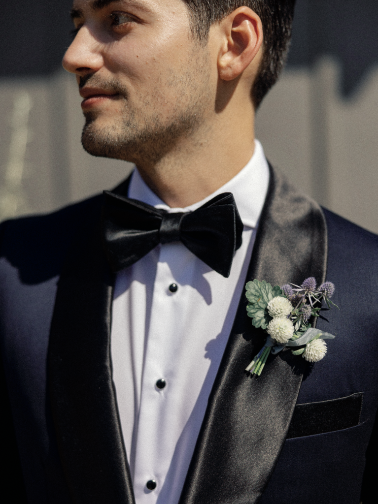 Small boutonniere with white and purple flowers rests on a groom's tuxedo during his Napa Valley wedding.