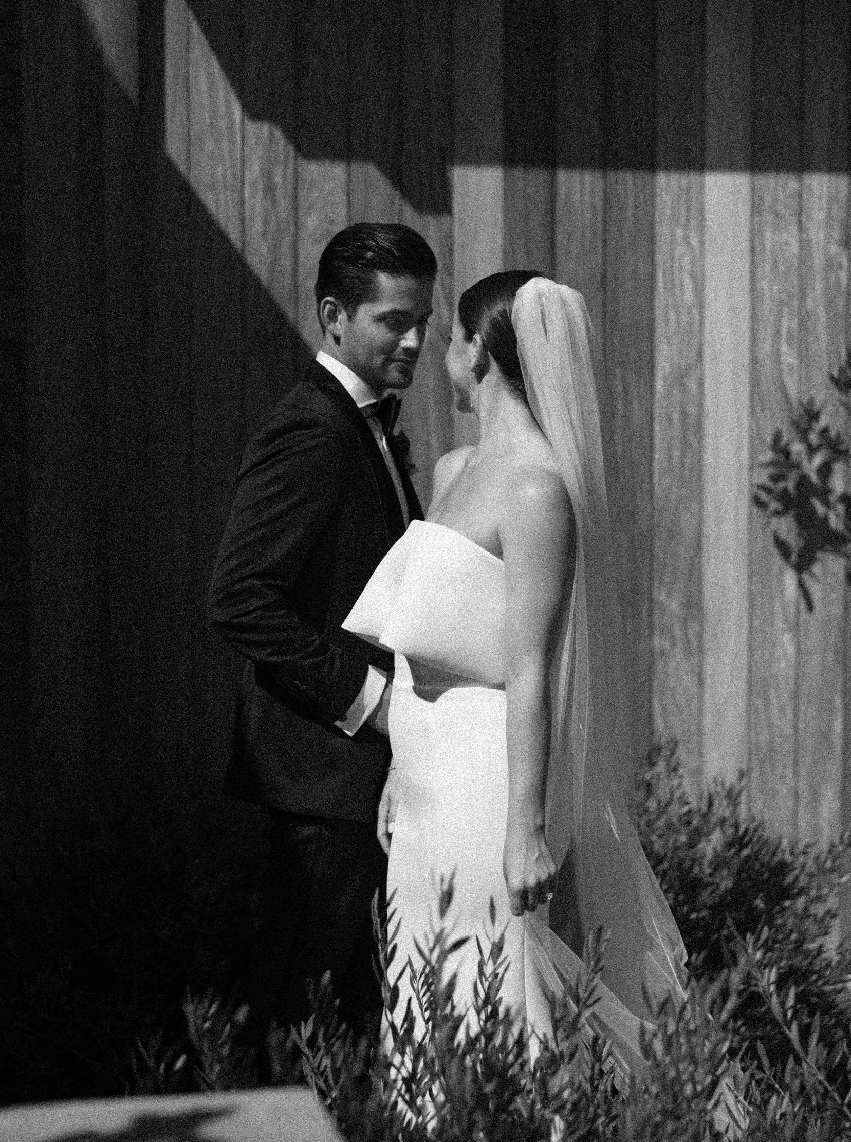 Black and white editorial wedding photograph of bride and groom. Groom is wearing a black tuxedo and standing int he shadow. Bride is wearing a white wedding dress and standing in the sun. Yin and Yang wedding photos.