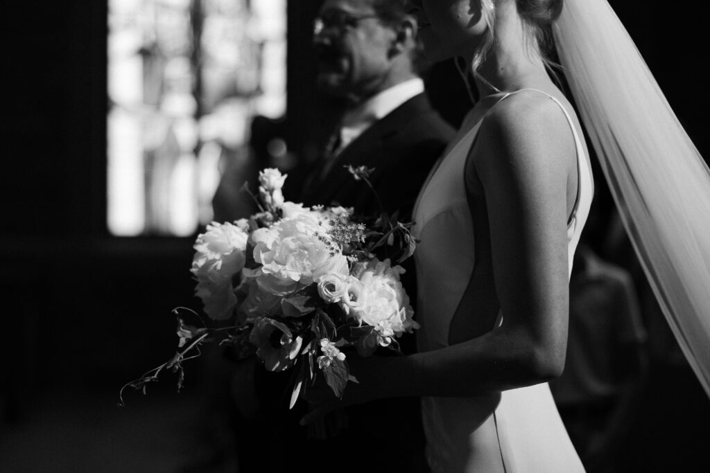 Black and white wedding photo of bride with white flowers walking down the asile.