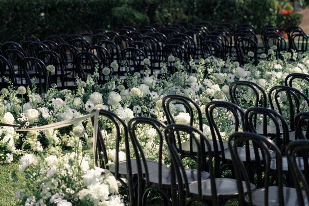 Sunlight streams through while flowers that go down the aisle of an empty wedding ceremony scape.