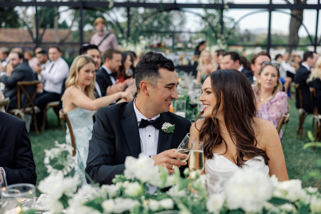 Bride and groom smile at each other while toasting during wedding speeches as photographed by Kay Cushman.