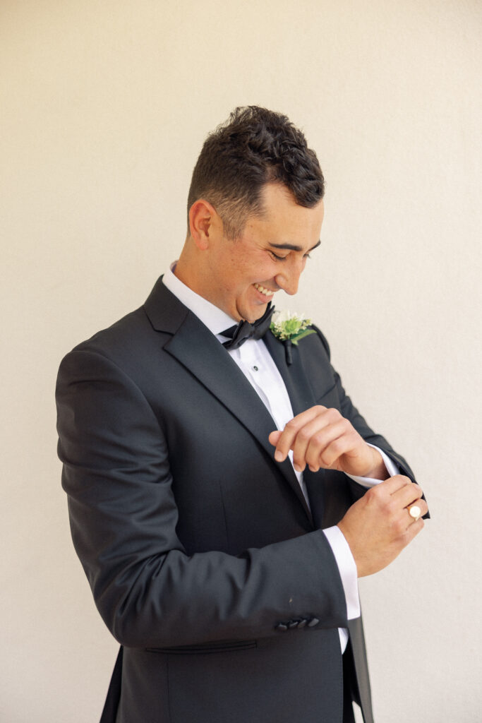 Groom smiles while fixing his cufflinks before seeing his bride on his wedding day at the Inn at Rancho Santa Fe.